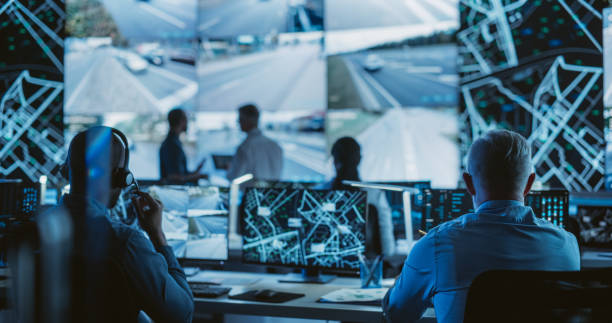 istock Dark Room with Multiethnic Specialists Working on Desktop Computers. Big Digital Screen Shows Surveillance Satellite Data, City Map, and CCTV Traffic Footage Reports 1553000187