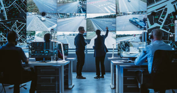 istock Traffic Commission Project Manager and Road Planning Department Computer Science Engineer Talking while Using Big Digital Display in a Monitoring Room. Screen Showing a Cluster of Live Traffic Feeds 1553002310