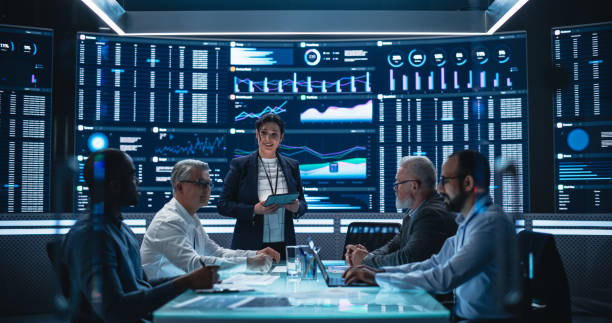 istock Diverse Team Of Data Scientists and Software Developers Discussing Reports in Monitoring Room with Analytics Feed on Big Digital Screen. Female Leading Artificial Intelligence Company Board Meeting 1553003388