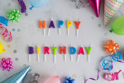 Happy Birthday cake candles letters with colorful balloons, cone hats, bows, and ribbons. Birthday party flat lay composition. Top view invitation concept frame.