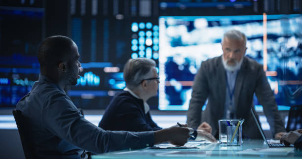 istock Diverse Group of Cybersecurity Experts Monitoring an Active Operation with Satellite Tracking Technology. Black Male Specialist Pitching an Idea for Tracking a Target Vehicle in Urban Terrain 1553008364