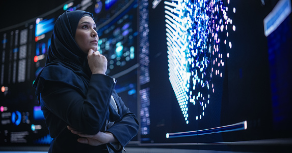Portrait of a Smart Focused Middle Eastern Software Engineer Analyzing Neural Network Big Data on a Digital Screen. Young Arab Woman in Hijab Working in an Innovative Internet Service Company