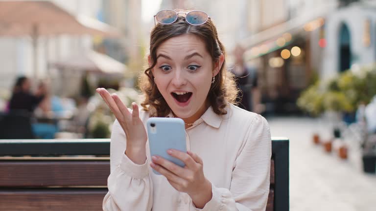 Amazed woman use smartphone celebrating win good message news lottery jackpot victory in city street