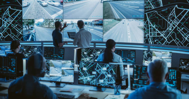 High-Tech International Logistics Office with Multiethnic Specialists Using Satellite Technology to Track a Fleet of Delivery Vehicles on a City Map. Large Display Shows Real-Time CCTV Feed and Report oficina de logística internacional de alta tecnología con especialistas multiétnicos que utilizan tecnología satelital para rastrear una flota de vehículos de entrega en un mapa de la ciudad. la pantalla grande muestra la alimentación e informe de cc