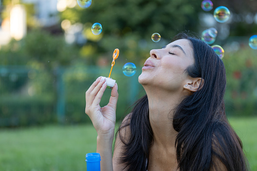 Pretty young woman is playing bubble wand at public park.