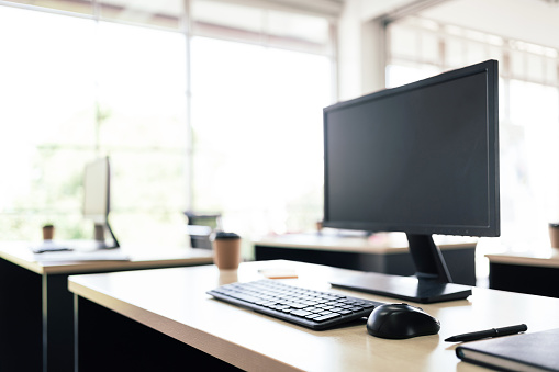 Mockup of modern personal desk office with monitor display, keyboard, mouse, notebook, pen and a paper coffee cup on the table in modern workspace. Image with copy space.