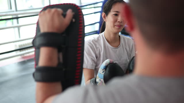 Young Asian woman training with male instructor at boxing gym