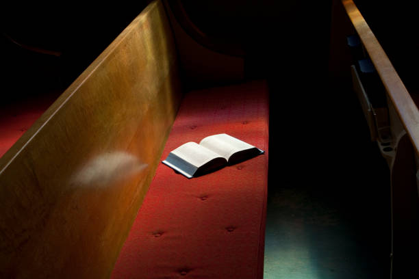 Open Bible Lying on Church Pew in Narrow Sunlight Band Open bible on top of a padded church pew.  Narrow band of light on book, but rest of church is dark.- See lightbox for more   pew stock pictures, royalty-free photos & images