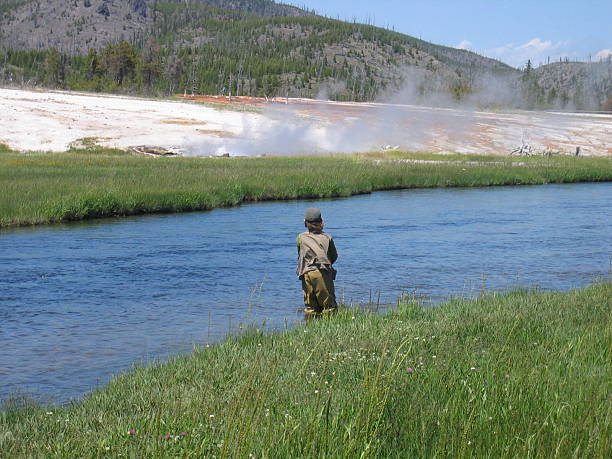 boy pesca con mosca en yellowstone con géiser en el fondo - río firehole fotografías e imágenes de stock