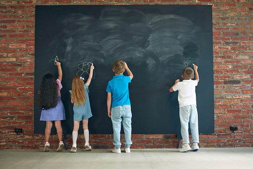 Little boys and girls, children drawing on blackboard, spending time together, studying, learning, playing. Concept of business, education, lessons, games and study, psychology. Ad