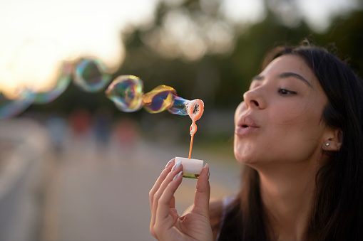 a woman at seaside blowing bubbles with romantic sunset sky