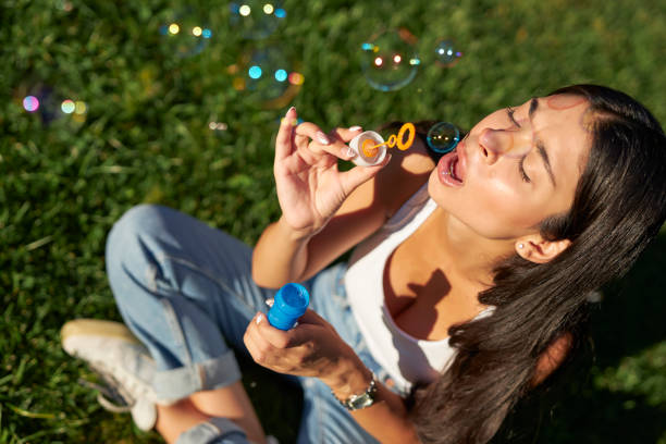 istock young brunette sitting at park and using bubble wand 1553134137