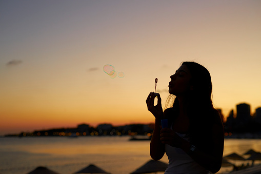 a woman at seaside blowing bubbles with romantic sunset sky