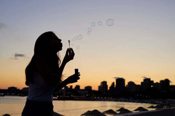 a woman at seaside blowing bubbles with romantic sunset sky