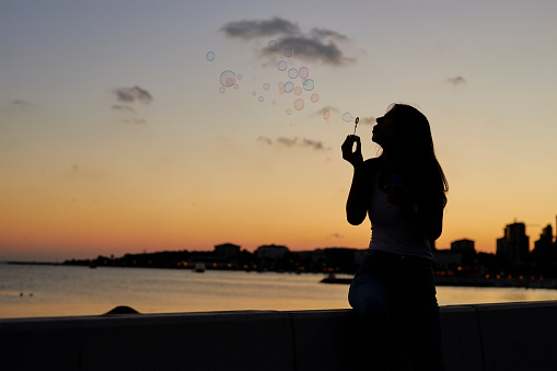 a woman at seaside blowing bubbles with romantic sunset sky