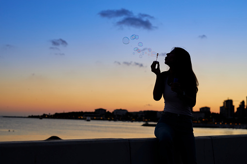 a woman at seaside blowing bubbles with romantic sunset sky