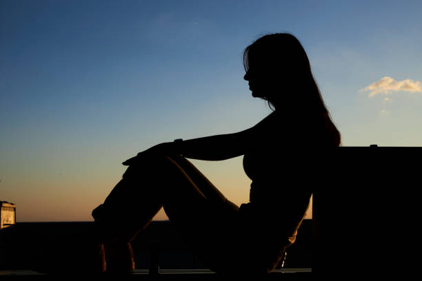 beautiful silhouette of a young lady sitting in peace at a park bench near seaside