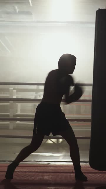 Kickboxing, woman fighter trains his punches, beats a punching bag, training day in the boxing gym, strength fit body, the girl strikes fast, vertical video.