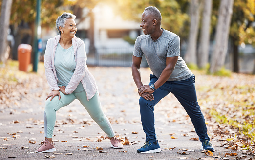 Exercise, stretching and senior couple in park for healthy body, wellness and workout outdoors. Retirement, sports and happy man and woman stretch legs for fitness, training and warm up for wellbeing