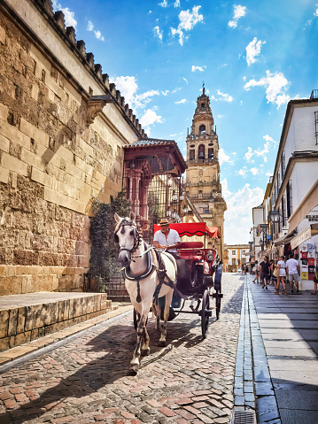 Cordoba, Spain - June 17, 2023: Horse carriage passing in front of the Cordoba mosque on a calm and sunny day. Spain. The Mosque-Cathedral of Cordoba, Mezquita. It was built by the Visigoths in 711 and it was converted to a Roman Catholic church, in the 16th century. It is one of the oldest structures still standing from the time Muslims in the late 8th century. Its a World Heritage Site since 1984.