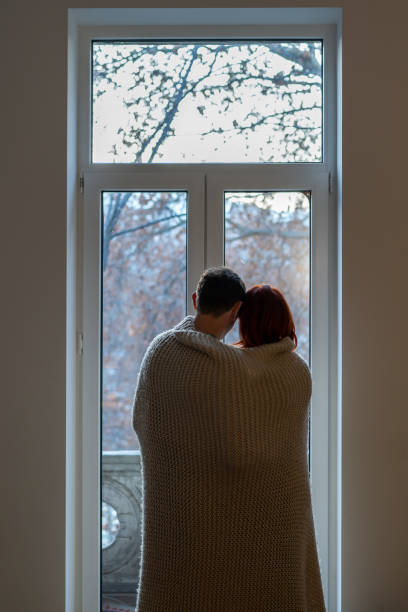 istock Couple wrapped in blanket looking out window 1553166597