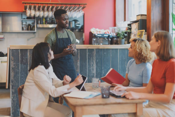세 명의 다민족 프리랜서 여성의 테이블에서 주문을 받는 아프리카계 미국인 바 주인 - four people service customer team 뉴스 사진 이미지