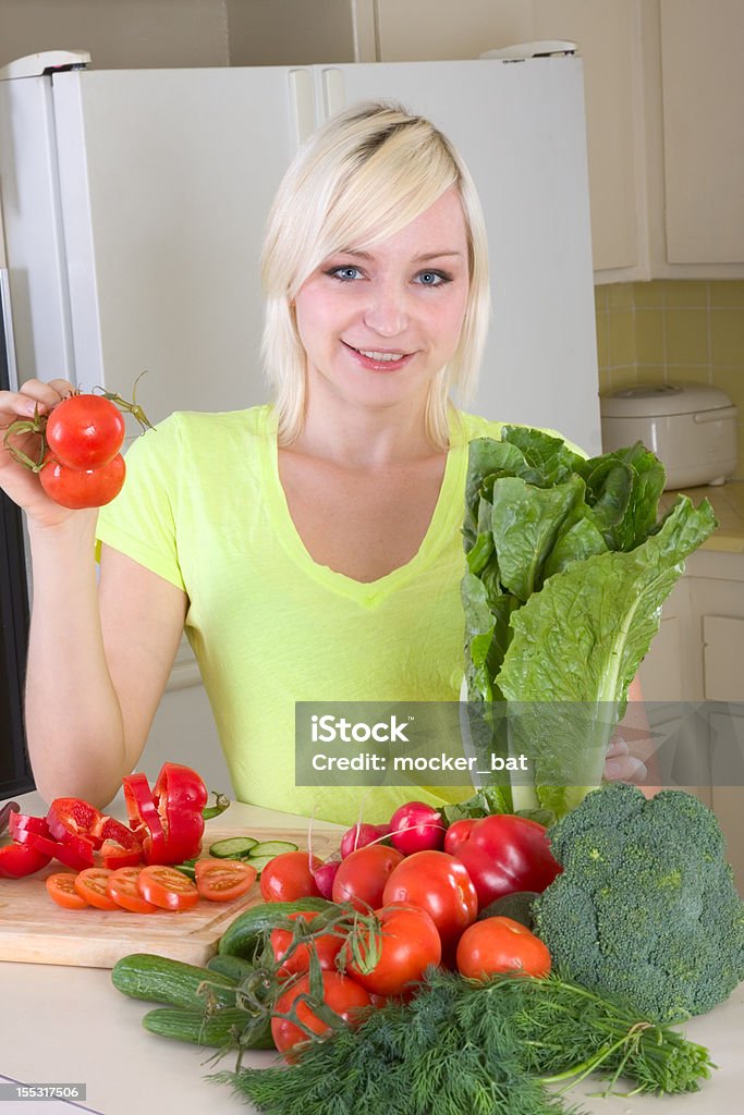 Giovane donna bionda mette con verdure in cucina - Foto stock royalty-free di 25-29 anni