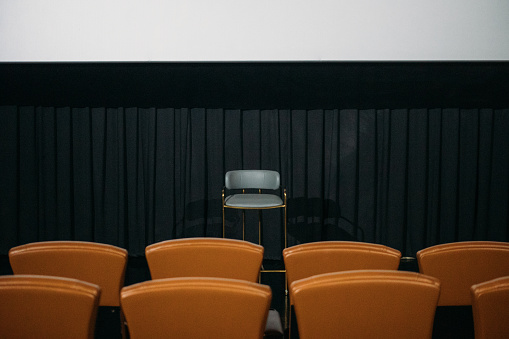 An empty chair in front of a row of seats in an auditorium - stock photo