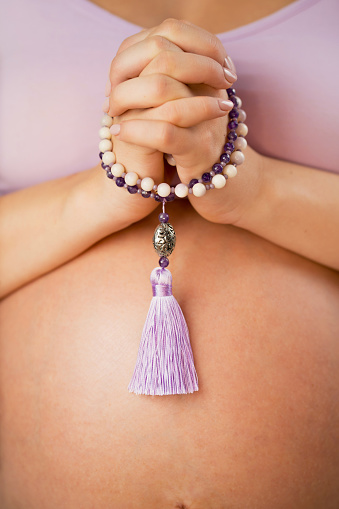 Woman, lit hand close up, counts Malas, strands of gemstones beads used for keeping count during mantra meditations.
