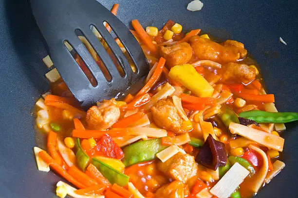 Asian food with chicken and vegetables being fried in a wok.