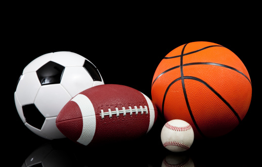 A group of sports balls on a black background including a baseball, an American football, a basketball and a soccer ball