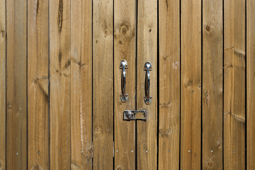 Close-up of a brown wooden gate with shiny metal handles.