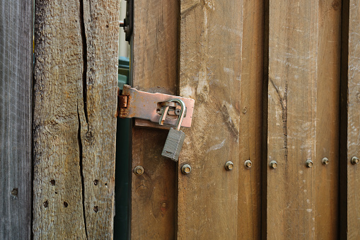Detail of a wooden door with an old unlocked padlock.