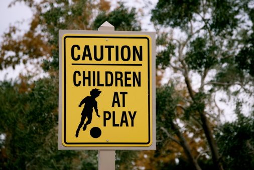 A yellow sign with a child playing soccer with black text that says: