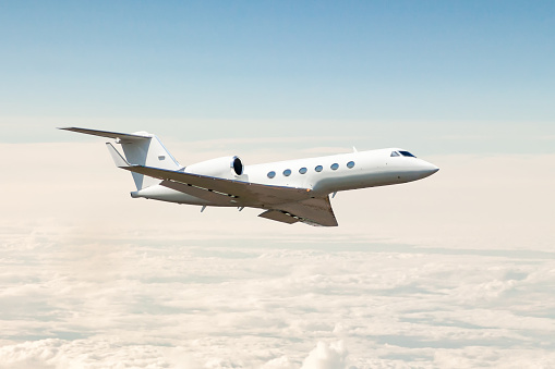 White luxury private jet flying in the air above the clouds