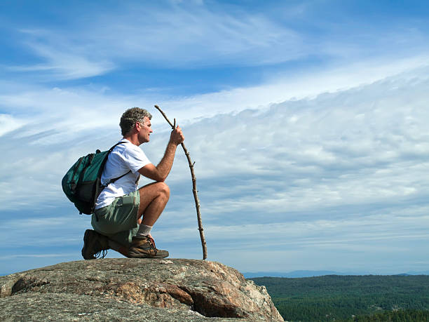 Mature adult caucasian male with walking stick and backpack at top of mountain overlooking wilderness