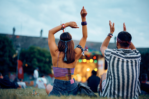 Back view of couple listening music in front of a stage during open air summer festival.