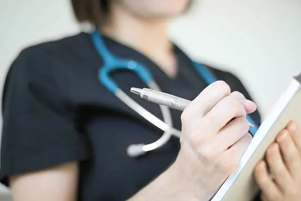 Health professional wearing stethoscope writing on pad of paper