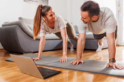 Couple working out together at home, doing online yoga course, exercising arm plank pose