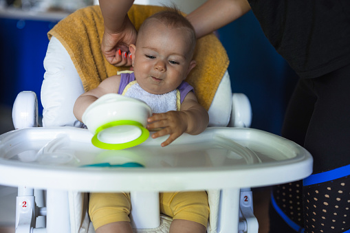 Mother helping her infant be comfortable in a high baby chair during a meal