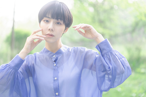 Young Asian woman's beauty portrait.  she is standing in forest. sunlight filtering through trees.