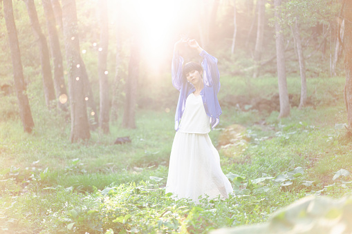 A young Asian woman wearing white clothes is standing in a forest  with a stream running through it. Backlight.
