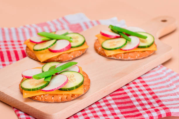 Light Breakfast. Quick and Healthy Sandwich. Fresh Cucumber and Radish with Green Onions and Cheese on Crispy Cracker on Wooden Cutting Board