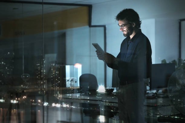 istock Business man, tablet and smile in office, online browsing or internet scroll by window with city lights at night. Technology, happiness and professional person with touchscreen for research deadline. 1553289755