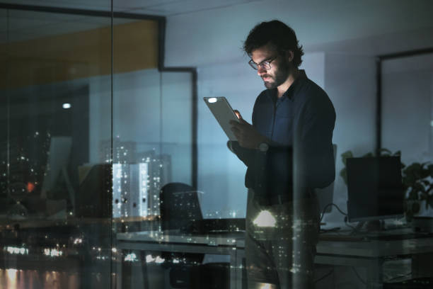 istock Night, news or businessman with tablet in office to search digital technology, data analytics or global media. City view, entrepreneur or focused person typing on iot dashboard or networking online 1553289757