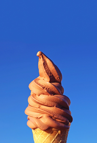 Chocolate Soft Serve Ice Cream Cone Against Sunny Vibrant Blue Sky