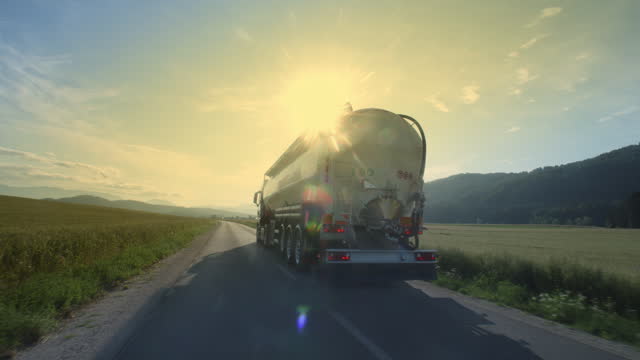 Sunlit oil tanker driving on road at sunset back view tracking shot