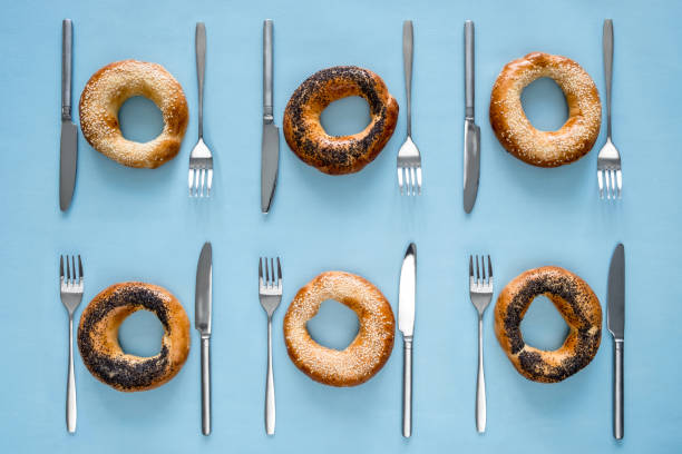 Small dry bagels with poppy seeds and sesame with cutlery on blue background top view