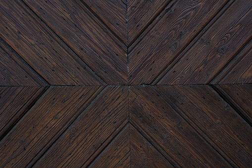 Cutout of an ancient wooden door showing pattern of dark brown wooden planks that  are symmetrical both vertically and diagonally. Suitable as background with a lot of copy space.