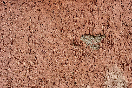 Terracotta colored decorative plaster with damage. Abstract background.